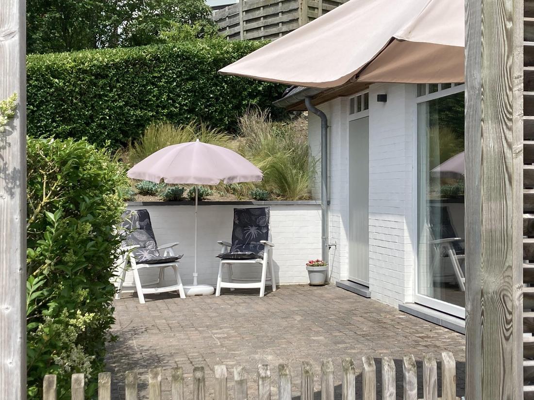 Bestraat terras met eettafel, stoelen en een parasol.